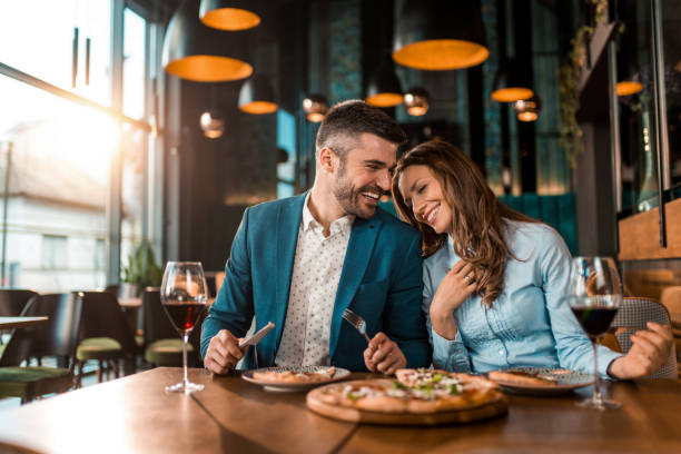 Cheerful elegant couple eating pizza together and having fun in a restaurant.